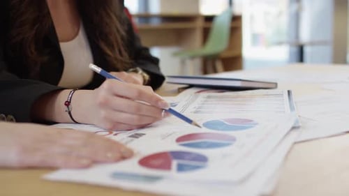 Woman Reviewing Financial Charts with Pencil in Office