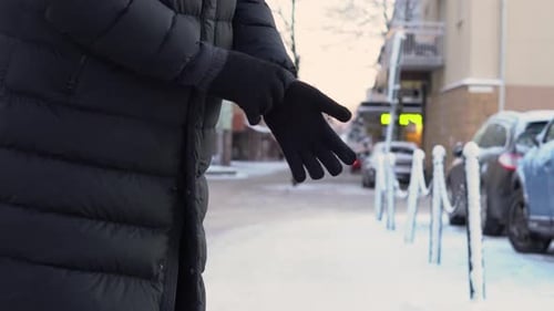 Man putting on black gloves in a snowy city street during cold winter weather