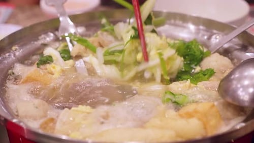 Detail of chopsticks removing vegetables from a boiling sukiyaki pot