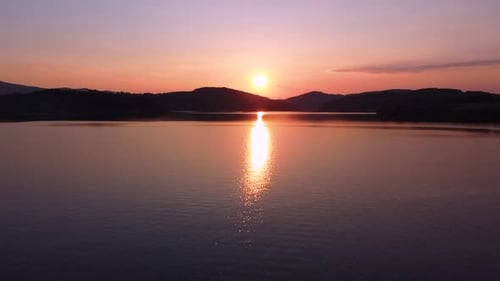 Couple sitting on the wall by the lake during sunset; drone aerial shot