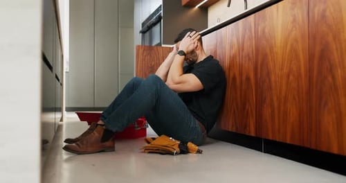 Headache, plumbing and problem with man in kitchen of home for maintenance or repair project