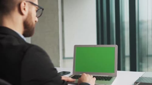 A laptop with a chromakey screen on a table in an office with panoramic windows