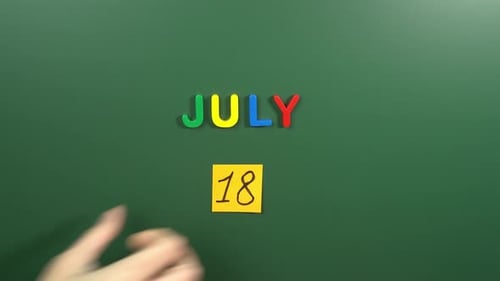 Hand sticking a sticker 18 July calendar day on school board. 18 date of July. Eighteenth day