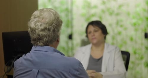 Senior male patient sitting in medical office talking to female doctor during healthcare