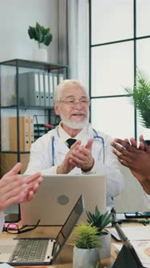Senior Doctor Applauds Colleagues Around Conference Table