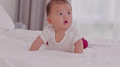 Adorable Baby Lifts Head on White Bed