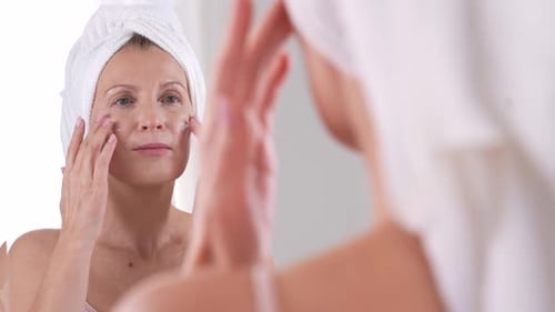 Woman Applies Face Cream in Bathroom Mirror