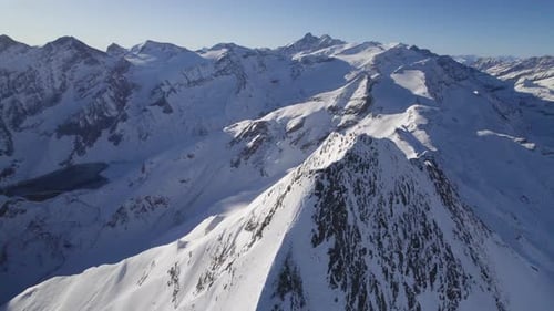 Drohne kreist an einem sonnigen Tag um einen verschneiten Berggipfel mit einer verschneiten Berglandschaft dahinter