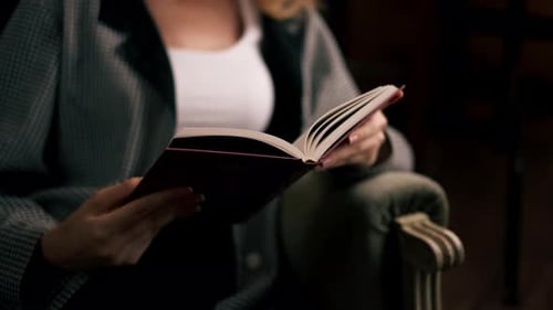 Nahaufnahme in einer schönen Buchhandlung sitzt ein junges Mädchen mit langen Haaren auf einem Stuhl und liest einen Buchabend