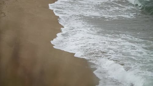 Side view of waves deepening the sand, shot in slow motion with tele lens from a higher point of vie
