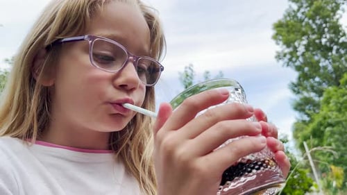 A Blonde Eightyearold Girl Drinks a Sweet Carbonated Drink From a Glass The Child Drinks Sweet