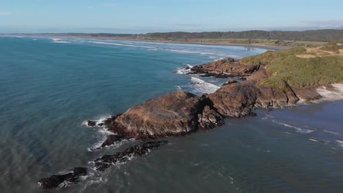 Aerial view of rocky shore of New Zealand during sunset in 4K shot over the ocean flying towards the