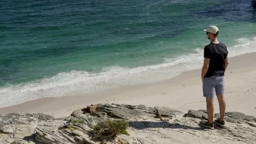 Man standing on a cliff facing the ocean. Pan handheld