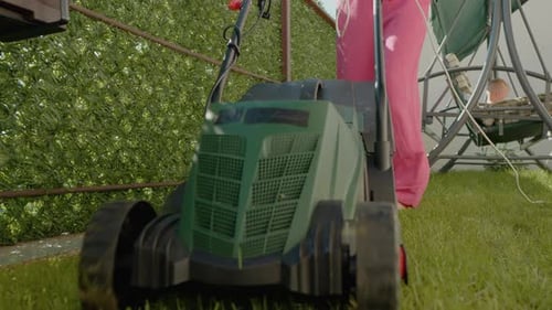 Mowing the lawn with an electric mower while caring for the backyard