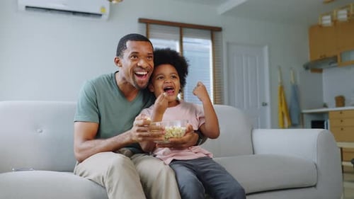 Father and Child Excitedly Watching TV With Popcorn