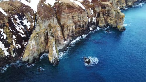 Flying Over Rocky Coastline Cliffside with Snow Over Blue North Atlantic Ocean Water at Spring