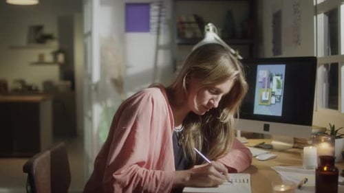 Woman Writing Design Ideas in Notebook at Desk