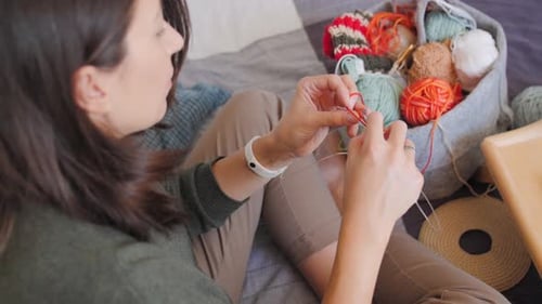 Woman Knitting with Yarn on Bed at Home