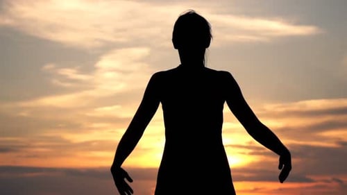 Silhouette of woman stretching arms at colorful sunset
