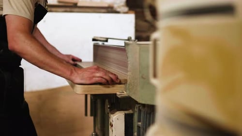 Skilled carpenter shaping wood with a planer in a workshop during daylight hours