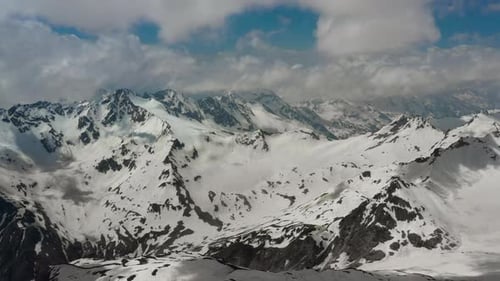 Air flight through mountain clouds over beautiful snow-capped peaks of mountains and glaciers.