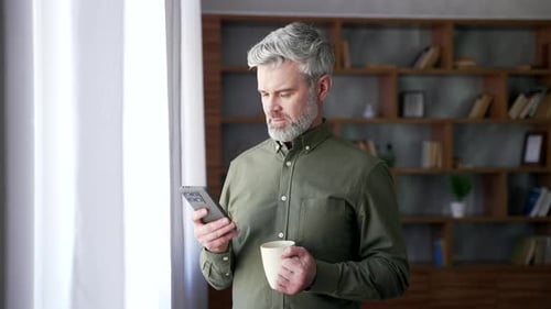 Man with Mobile Phone and Coffee Stands Indoors
