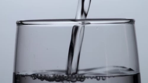 Close Up Of Drinking Water Being Poured Into A Glass On The Light White Screen Background
