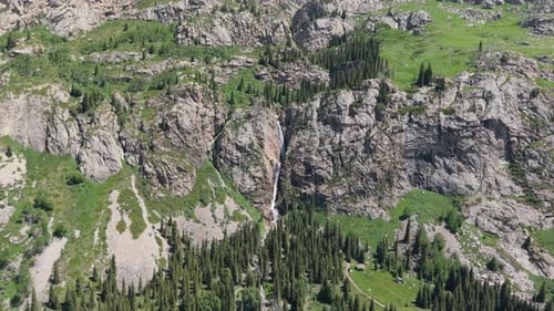 Waterfall Cascading Down Rocky Mountainside in Lush Green Valley