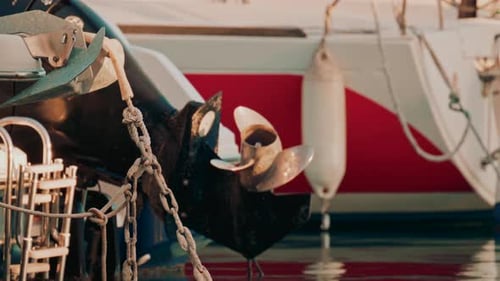 Cinematic shot of a boat propeller near a red hull, reflecting vibrant colors on the water surface