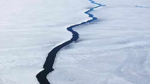 Aerial View of a Crack with Water in the Icy Frozen Surface Sunny Spring Day