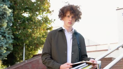 Young Redhead Curly Student Holds Books Posing with Backpack Near College Building Outdoor Smiling