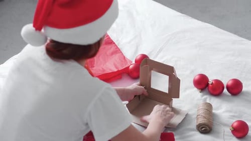 Person Assembling Christmas Gift Box with Ornaments