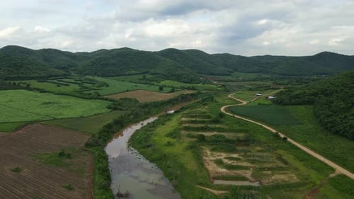 Aerial footage tilting from a gorgeous landscape down to the canal and farmland, dirt road on the ri