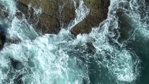 Powerful ocean waves clash against the rocky shore.