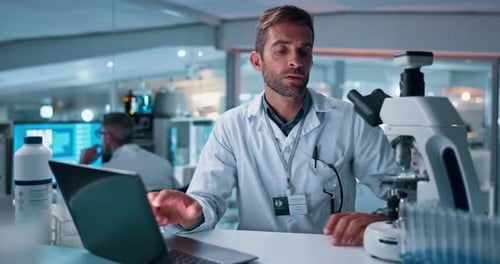 Scientist Using Microscope and Laptop in Lab