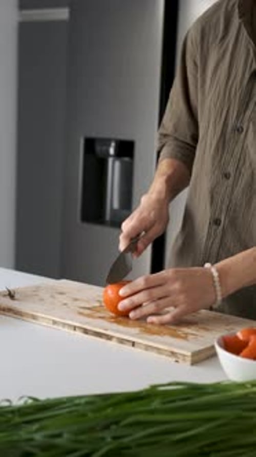 Person cutting tomato on a board in kitchen