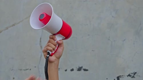 Close-up of hand raising megaphone surrounded by clenched fists during public protest