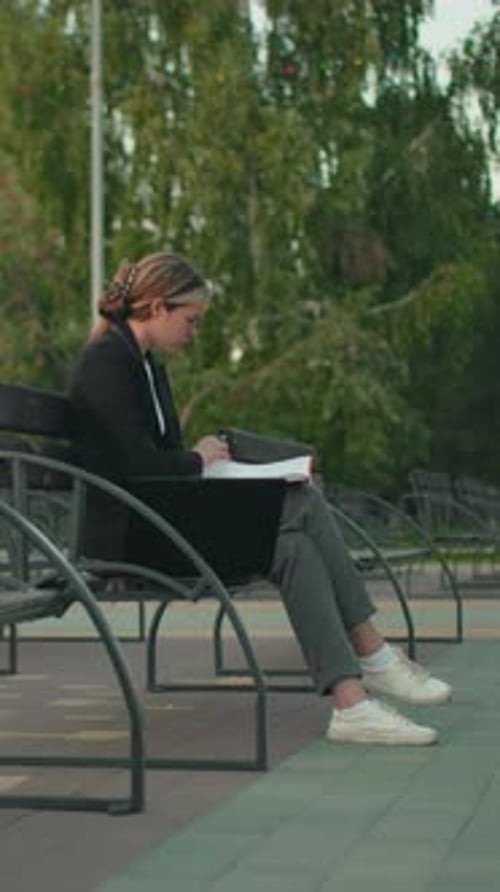 Young Woman Working Outdoors with Folder and Laptop in Tranquil Park Setting