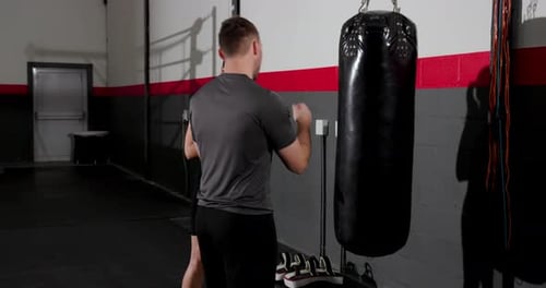 Male trainer tapping heavy bag and female trainee launching jabs for timing drill at boxing gym