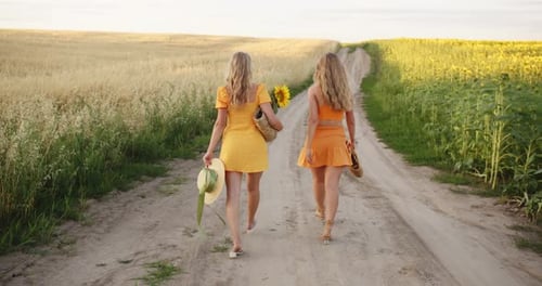 Two Blondes with a Bouquet of Flowers Walk Across the Field