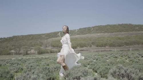 Beautiful young woman in white dress runs into field