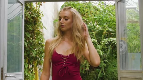 Fit swimwear model walking through a botanical garden, wearing a red bikini one piece.