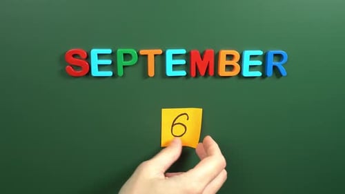 Hand sticking a sticker 6 September calendar day on school board. 6 date of September. Sixth day