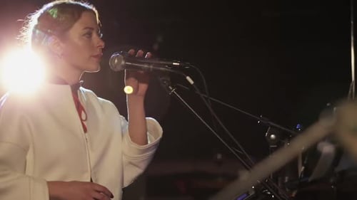 Woman Singing Into Microphone on Stage at Night