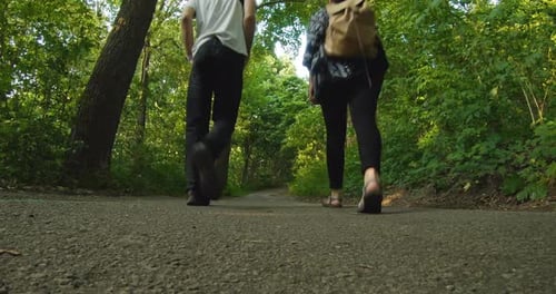 Man and woman walk together down a pathway in the woods. The forest is green and a soft wind blows.