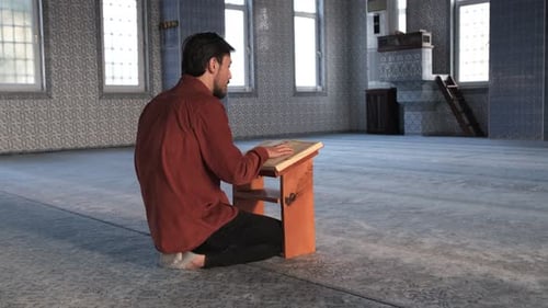 Seitenansicht eines bärtigen Mannes, der in der Moschee auf einem Tisch sitzt und das islamische Koranbuch liest, eine Religion