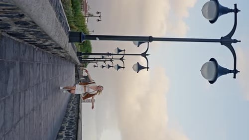 Woman Runs Along the Sidewalk Under a Cloudy Sky Passing By City Street Lights