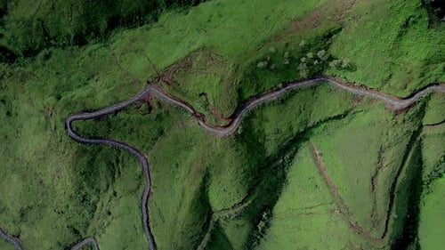 Drone footage of a winding mountain road cutting through lush green hills.