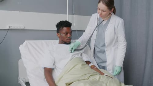 Doctor Using Stethoscope while Examining Patient in Hospital Bed
