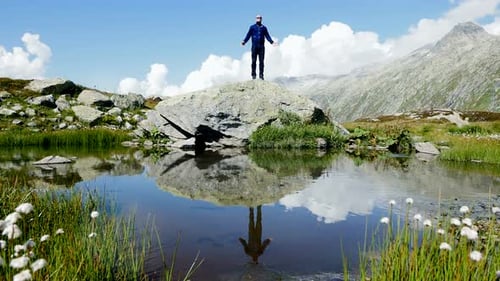 Man Stands on Rock Outcrop Overlooking Mountain Lake